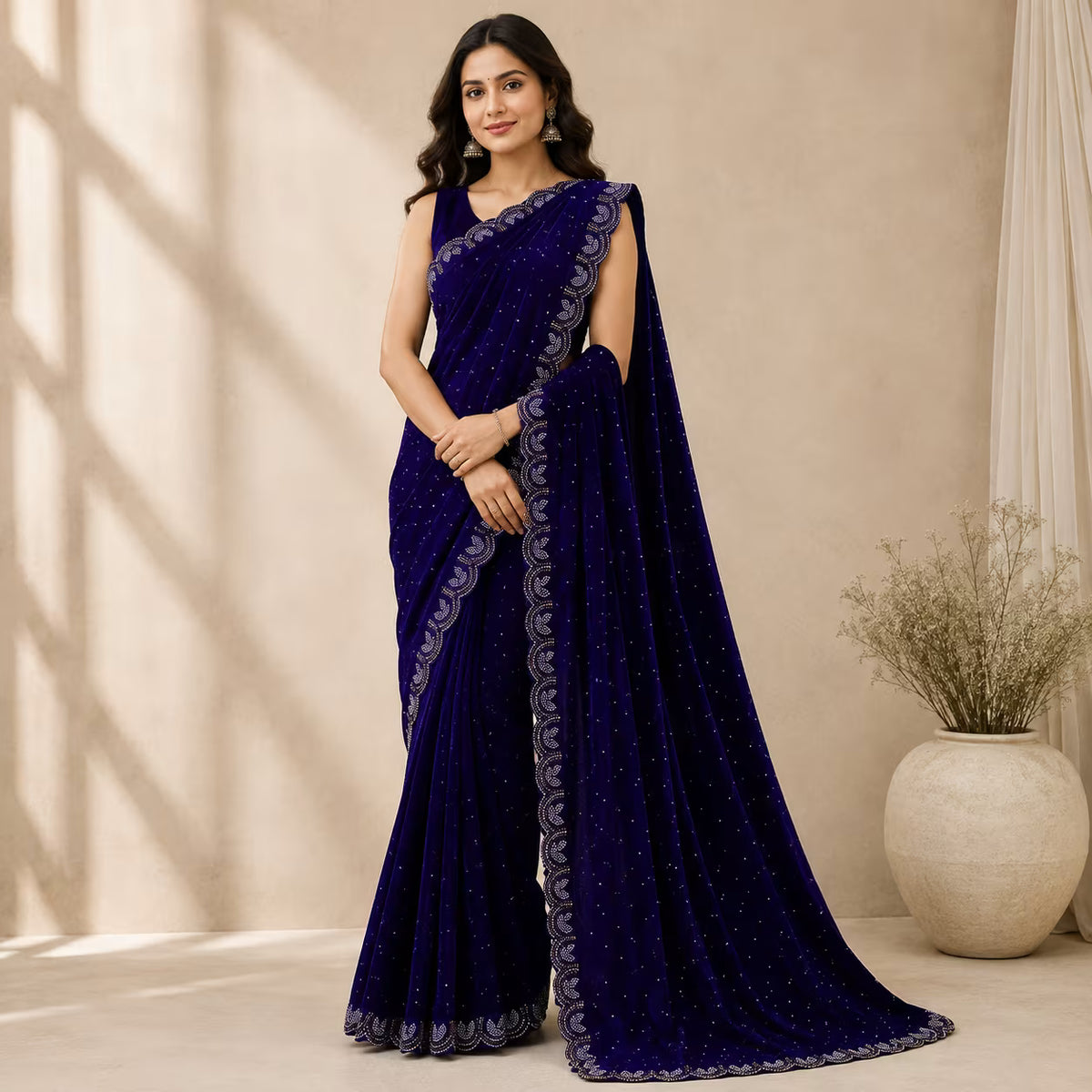 A woman models a deep navy blue saree with intricate silver embroidery and a matching embroidered border, set against a warm beige background with soft window shadows.