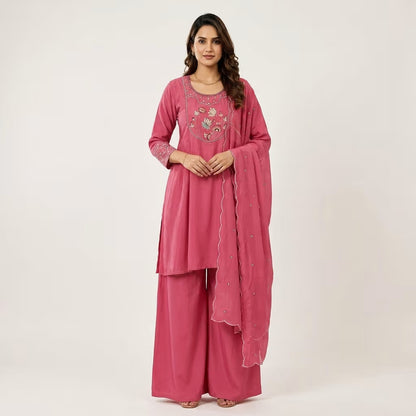 A woman modeling a pink traditional Indian outfit with a matching dupatta, featuring embroidered details on the chest and sleeves, set against a plain light background. Jukarsh Fashion
