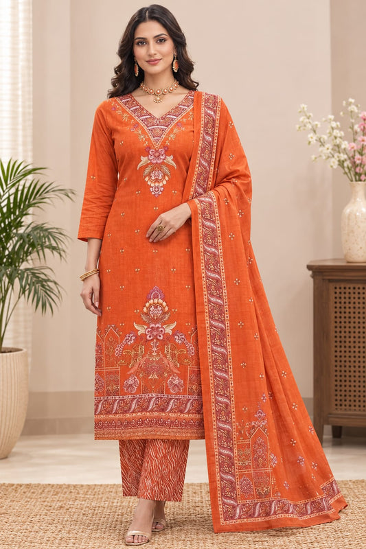A woman models an orange salwar kameez suit with intricate floral embroidery and a matching dupatta in a styled indoor setting.